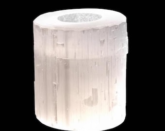 May include: A cylindrical selenite candle holder. The natural crystal is white and translucent, with visible vertical striations. The top has a circular opening for a candle. The background is black.