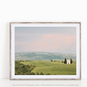May include: A photograph of a white chapel in a field of green rolling hills. The sky is a soft pink and blue.