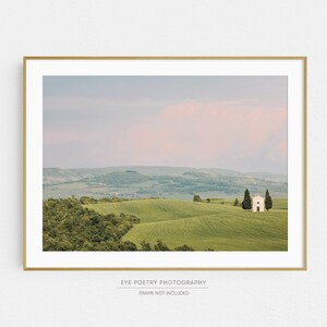 May include: A white building with a red roof sits on a green hilltop in a landscape of rolling hills. The sky is a soft pink and blue.