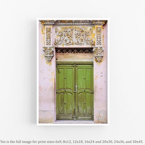 May include: A vintage green double door with ornate carvings above the door. The door is set in a pink building with faded paint.