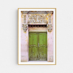 May include: A vintage green double door with ornate carvings above the door. The door is set in a pink building with faded paint.