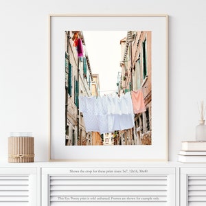 Pu&ograve; includere: Una fotografia di un vicolo stretto a Venezia, Italia. Lenzuola bianche sono appese a uno stendino teso tra gli edifici. Gli edifici sono dipinti in tonalit&agrave; di rosa e giallo.