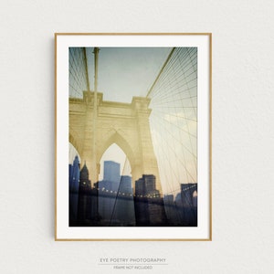 Puede incluir: Una fotograf&iacute;a de estilo vintage del puente de Brooklyn en la ciudad de Nueva York. El puente es de color amarillo claro y el fondo es de un azul brumoso con un patr&oacute;n de cuadr&iacute;cula. La imagen est&aacute; enmarcada en un marco de madera claro.