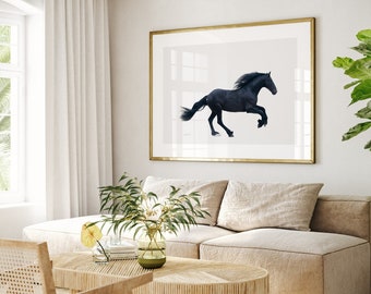 Può includere: Un cavallo nero che corre in un campo, incorniciato in una cornice dorata e appeso a una parete bianca sopra un divano beige. Il divano è in un soggiorno con una grande finestra e una pianta in vaso.