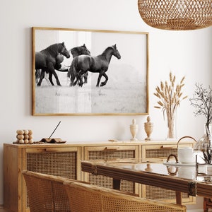 May include: Black and white photograph of four horses running in a field. The photo is framed and hanging on a wall above a wooden cabinet with woven cane doors.