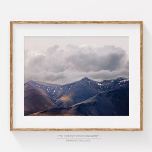Puede incluir: Una fotograf&iacute;a enmarcada de una cordillera con una gran nube esponjosa que cubre los picos. Las monta&ntilde;as son de color p&uacute;rpura oscuro con toques de marr&oacute;n y amarillo. El cielo es de color gris claro.