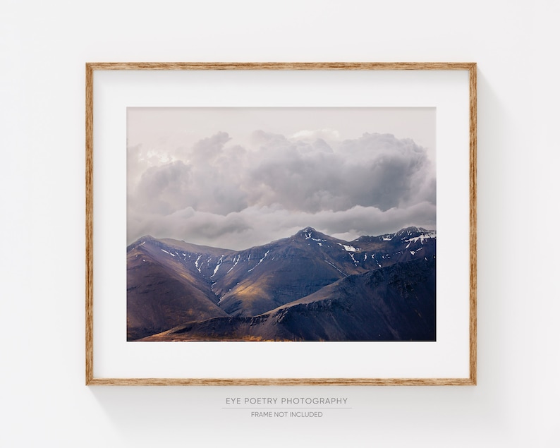 Puede incluir: Una fotograf&iacute;a enmarcada de una cordillera con una gran nube esponjosa que cubre los picos. Las monta&ntilde;as son de color p&uacute;rpura oscuro con toques de marr&oacute;n y amarillo. El cielo es de color gris claro.