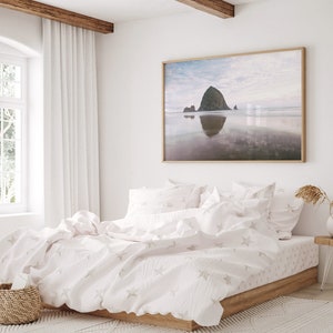 May include: A white bed with a white duvet cover and white pillowcases. The duvet cover has a subtle star pattern. The bed is in a bedroom with a large window and a framed print of a beach scene on the wall.