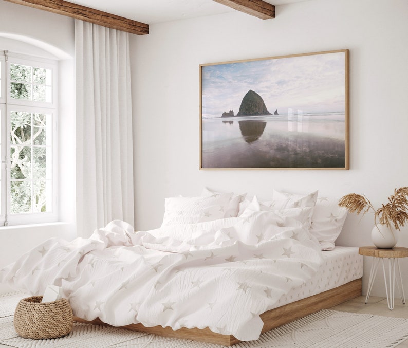 May include: A white bed with a white duvet cover and white pillowcases. The duvet cover has a subtle star pattern. The bed is in a bedroom with a large window and a framed print of a beach scene on the wall.