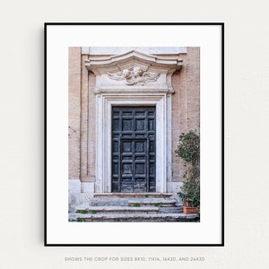 May include: A black wooden door with a decorative stone frame and a carved stone relief above it. The door is set in a building with a light beige facade.