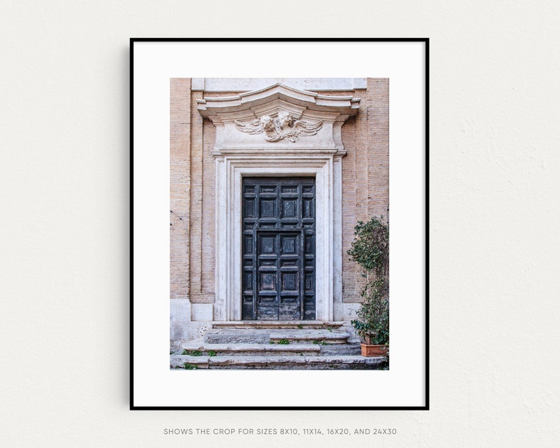 May include: A black wooden door with a decorative stone frame and a carved stone relief above it. The door is set in a building with a light beige facade.