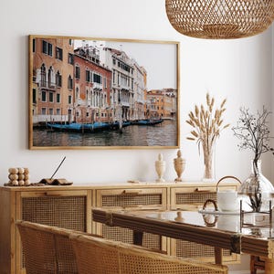 May include: A framed photograph of a canal in Venice, Italy. The photo shows a row of colorful buildings along the canal with gondolas floating in the water.