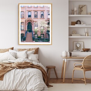 May include: A photograph of a row of brown brick townhouses with a green door and white flowers in front. The houses have white window frames and are in a city setting.