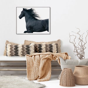 May include: A black horse with a flowing mane runs across a white background in a framed print above a light wood bench with a beige knitted throw and decorative pillows.