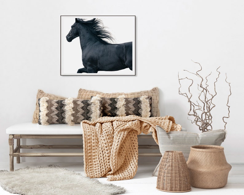 May include: A black horse with a flowing mane runs across a white background in a framed print above a light wood bench with a beige knitted throw and decorative pillows.