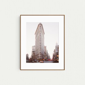 K&ouml;nnte beinhalten: Ein gerahmtes Foto des Flatiron Building in New York City. Das Geb&auml;ude ist ein dreieckiger Wolkenkratzer mit einem markanten spitzen Dach. Das Foto wurde aus der Perspektive der Stra&szlig;e aufgenommen und zeigt das Geb&auml;ude in seiner Gesamtheit.