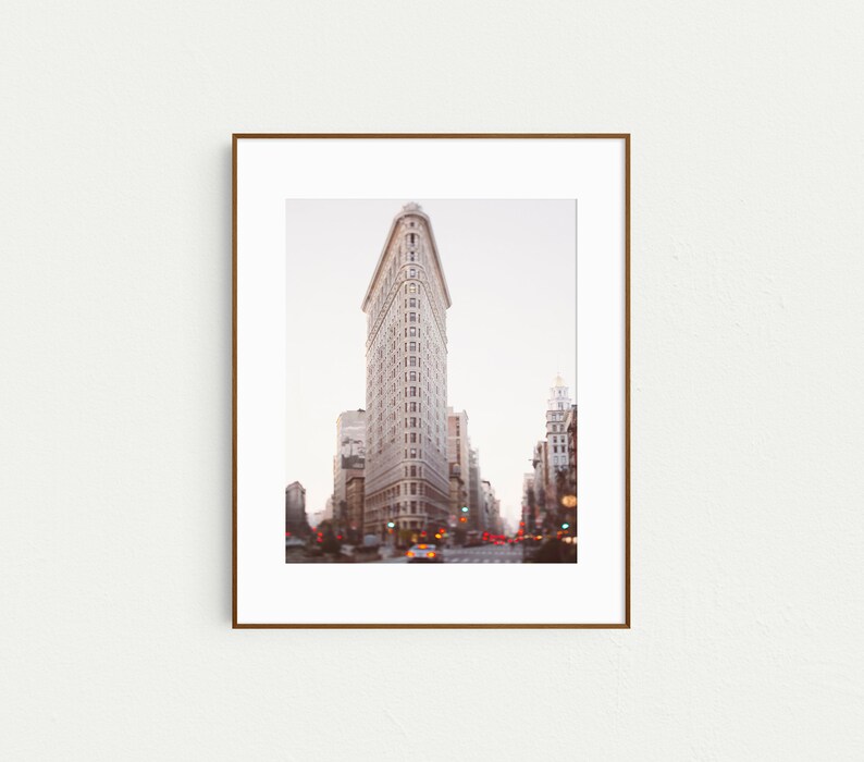 K&ouml;nnte beinhalten: Ein gerahmtes Foto des Flatiron Building in New York City. Das Geb&auml;ude ist ein dreieckiger Wolkenkratzer mit einem markanten spitzen Dach. Das Foto wurde aus der Perspektive der Stra&szlig;e aufgenommen und zeigt das Geb&auml;ude in seiner Gesamtheit.
