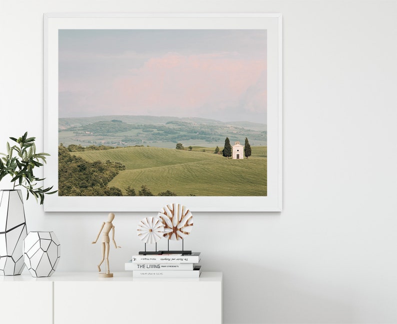 May include: A framed photograph of a white chapel with a pink sky in the background. The chapel is located on a grassy hill with rolling hills in the distance. The photo is framed in a white frame.