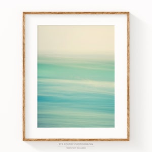 May include: Abstract art print with a blurred, horizontal, layered design in shades of blue, green, and white. The print is framed in a natural wood frame.