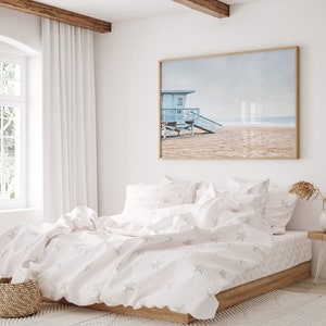 Peut inclure: Un lit blanc avec une housse de couette et des taies d'oreiller assorties &agrave; motifs d'&eacute;toiles blanches et grises. Le lit est dans une chambre avec une grande fen&ecirc;tre et une photographie encadr&eacute;e d'une sc&egrave;ne de plage au-dessus de la t&ecirc;te de lit.