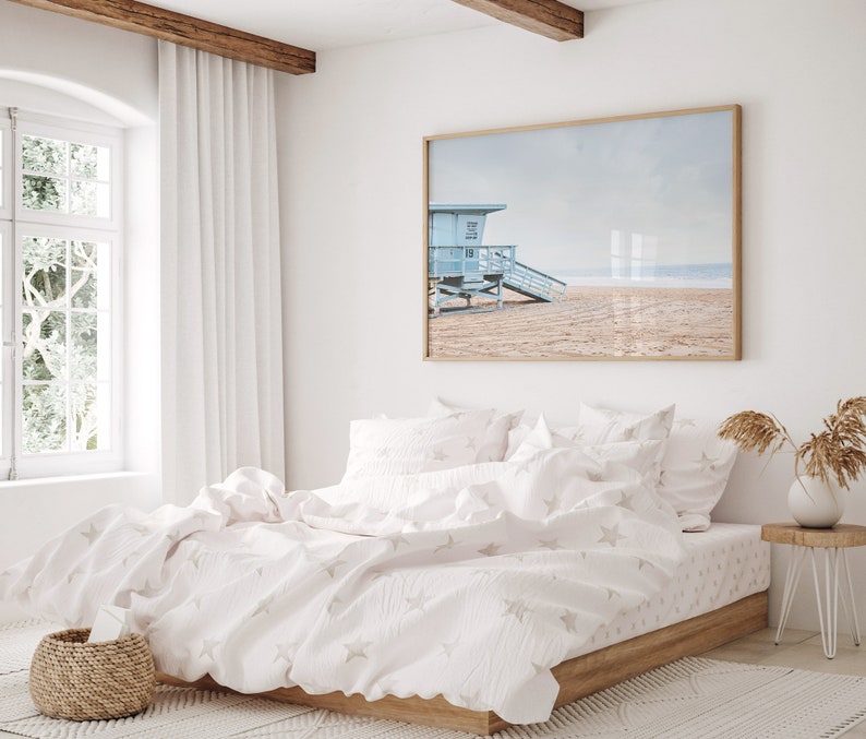Peut inclure: Un lit blanc avec une housse de couette et des taies d'oreiller assorties &agrave; motifs d'&eacute;toiles blanches et grises. Le lit est dans une chambre avec une grande fen&ecirc;tre et une photographie encadr&eacute;e d'une sc&egrave;ne de plage au-dessus de la t&ecirc;te de lit.