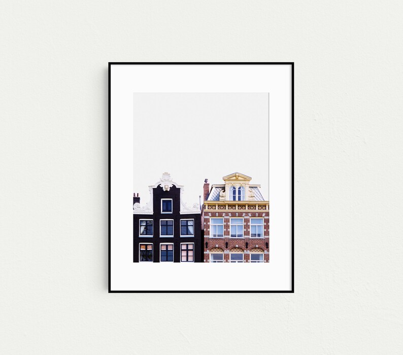 May include: A black and white photograph of two buildings in Amsterdam, Netherlands. The building on the left is black with white trim and the building on the right is red brick with a yellow trim.