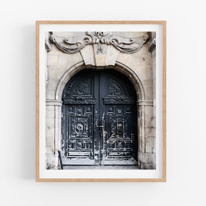 May include: A framed photograph of a weathered, dark blue double door with intricate carvings. The door is set in a stone archway with ornate details above.