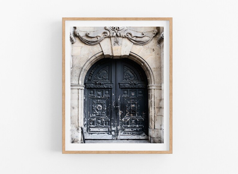 May include: A framed photograph of a weathered, dark blue double door with intricate carvings. The door is set in a stone archway with ornate details above.