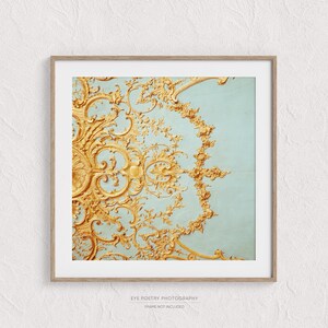 May include: A close-up of a gold ornate design on a light blue background. The design is intricate and detailed, with a floral motif. The background is a soft, muted blue.