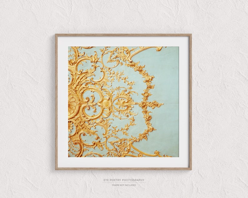 May include: A close-up of a gold ornate design on a light blue background. The design is intricate and detailed, with a floral motif. The background is a soft, muted blue.