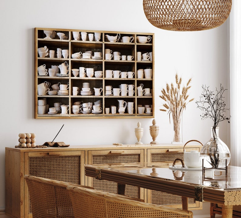 May include: A wooden cabinet with a glass-front cabinet above it. The cabinet is filled with white ceramic cups and saucers. The cabinet is in a room with a wooden table and chairs.