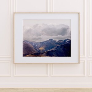 Puede incluir: Una fotograf&iacute;a enmarcada de una cordillera con un cielo nublado. Las monta&ntilde;as son de color azul oscuro y morado, y el cielo es de color gris claro con una gran nube blanca.