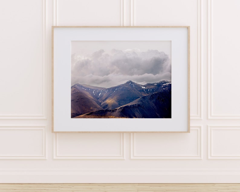 Puede incluir: Una fotograf&iacute;a enmarcada de una cordillera con un cielo nublado. Las monta&ntilde;as son de color azul oscuro y morado, y el cielo es de color gris claro con una gran nube blanca.