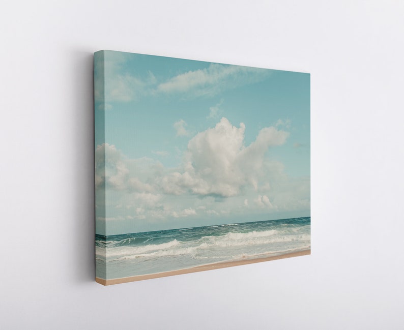 May include: A photograph of a blue sky with white clouds over a blue ocean with white waves crashing on the shore.