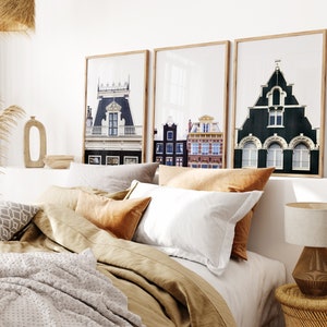 May include: Three framed prints of European cityscapes with colorful buildings and windows. The prints are hanging on a white wall above a bed with tan linen bedding and pillows.