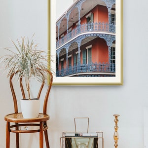 May include: A framed photograph of a red brick building with blue iron balconies. The building has multiple stories and is decorated with intricate details. The photograph is set against a white wall.