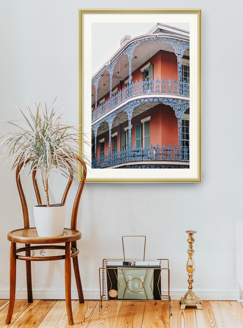 May include: A framed photograph of a red brick building with blue iron balconies. The building has multiple stories and is decorated with intricate details. The photograph is set against a white wall.