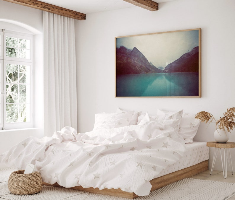 May include: A white bed with a white duvet cover and white pillowcases. The duvet cover has a subtle star pattern. The bed is in a bedroom with a large window and a framed photograph of a mountain lake.