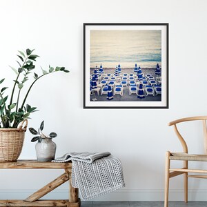 May include: A framed photograph of a beach scene with blue and white striped beach chairs and umbrellas. The chairs are arranged in rows on the sand, with the ocean in the background.