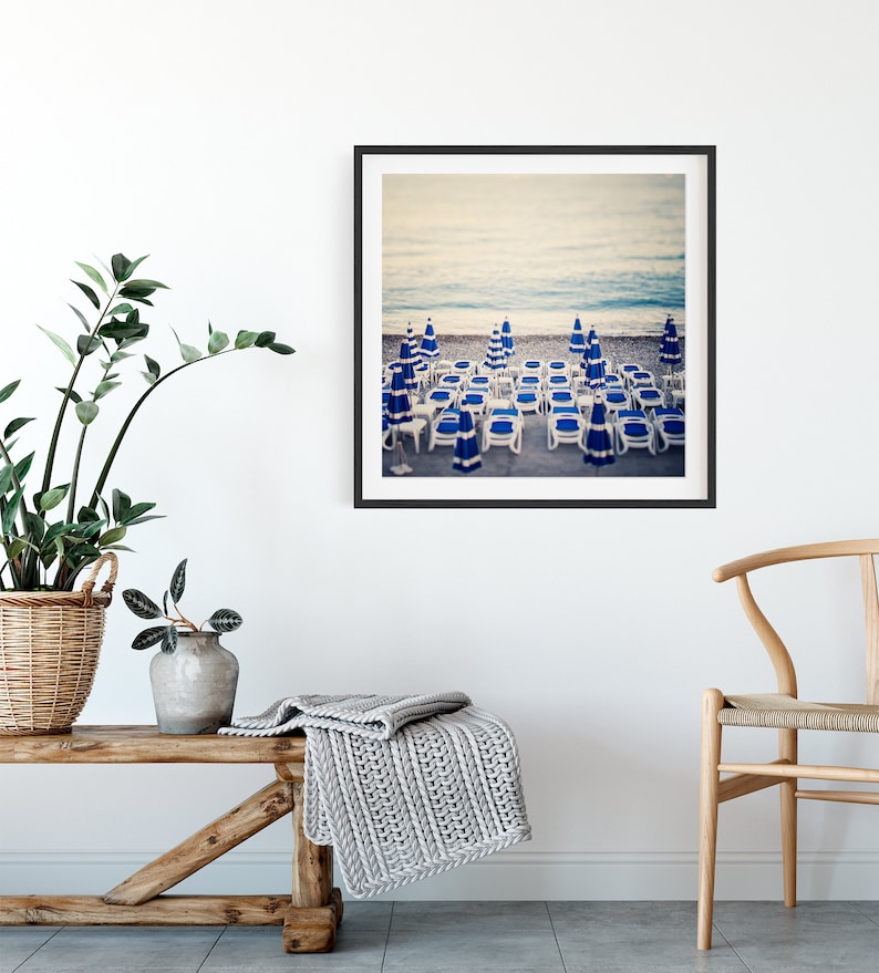 May include: A framed photograph of a beach scene with blue and white striped beach chairs and umbrellas. The chairs are arranged in rows on the sand, with the ocean in the background.