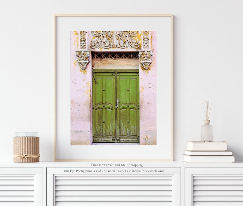 May include: A photograph of a green double door with ornate carvings above the door. The door is set in a pink building with peeling paint.