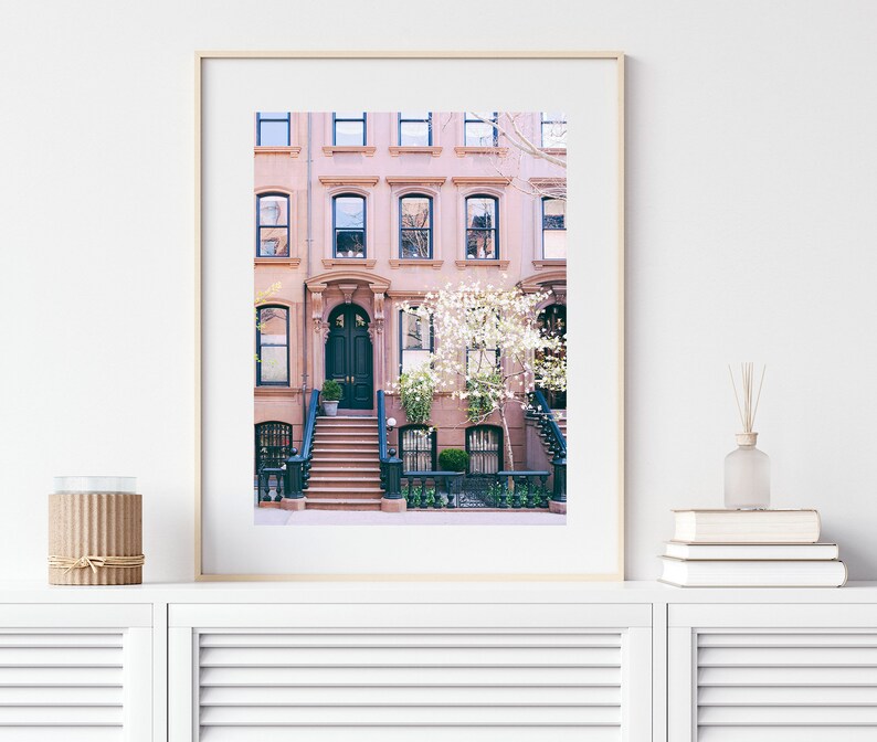 May include: A photograph of a pink brick row house with a black door and white flowers in front. The house has a stoop with steps leading up to the door.