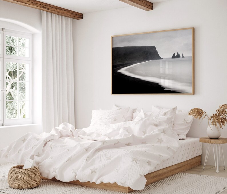 May include: A white bed with a white duvet cover and white pillowcases. The duvet cover has a subtle star pattern. The bed is in a bedroom with a large window and a black and white photograph of a beach scene hanging on the wall.