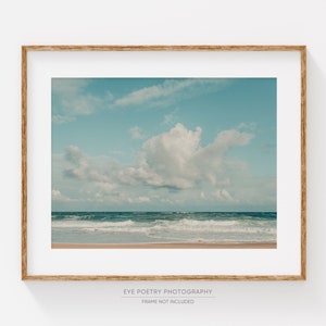 May include: A framed photograph of a beach scene with a large white cloud in a blue sky and waves crashing on the shore.