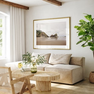 May include: A light beige sectional sofa with a wooden coffee table in a living room with a large framed photograph of a beach scene and a potted plant.