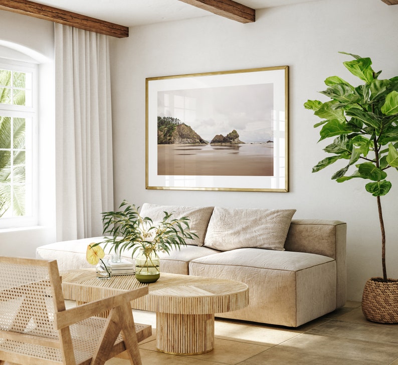 May include: A light beige sectional sofa with a wooden coffee table in a living room with a large framed photograph of a beach scene and a potted plant.