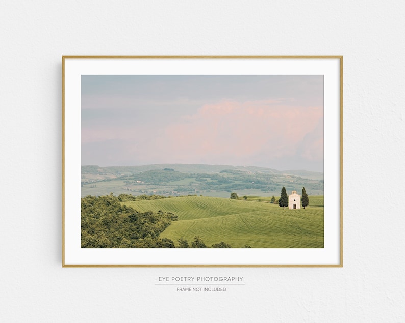 May include: A white building with a red roof sits on a green hilltop in a landscape of rolling hills. The sky is a soft pink and blue.