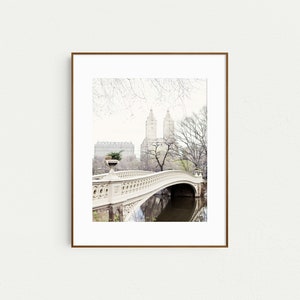 K&ouml;nnte beinhalten: Eine wei&szlig;e Steinbr&uuml;cke mit verzierten Details spannt sich &uuml;ber ein ruhiges Gew&auml;sser. Die Br&uuml;cke ist von B&auml;umen und hohen Geb&auml;uden im Hintergrund umgeben.
