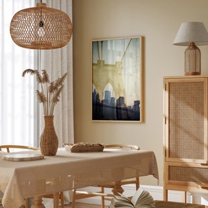 Puede incluir: Una mesa de comedor con un mantel beige, sillas de mimbre y una l&aacute;mpara colgante de mimbre colgando arriba. Una impresi&oacute;n enmarcada de un puente con una ciudad en el fondo cuelga de la pared. Un armario de madera con una puerta de rat&aacute;n tejido est&aacute; en el fondo.