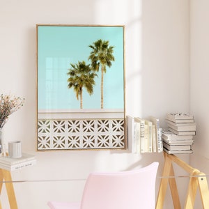 May include: A framed print of two palm trees against a light blue sky. The trees are silhouetted against a white wall with a decorative pattern.
